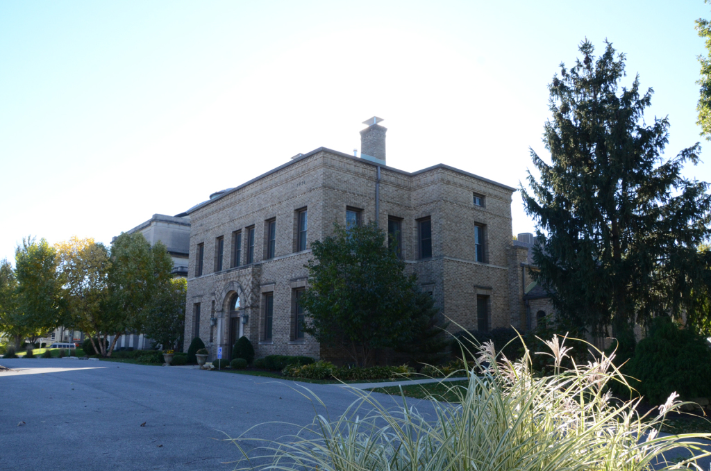 Large brick building with multiple windows, trees, and a clear sky.