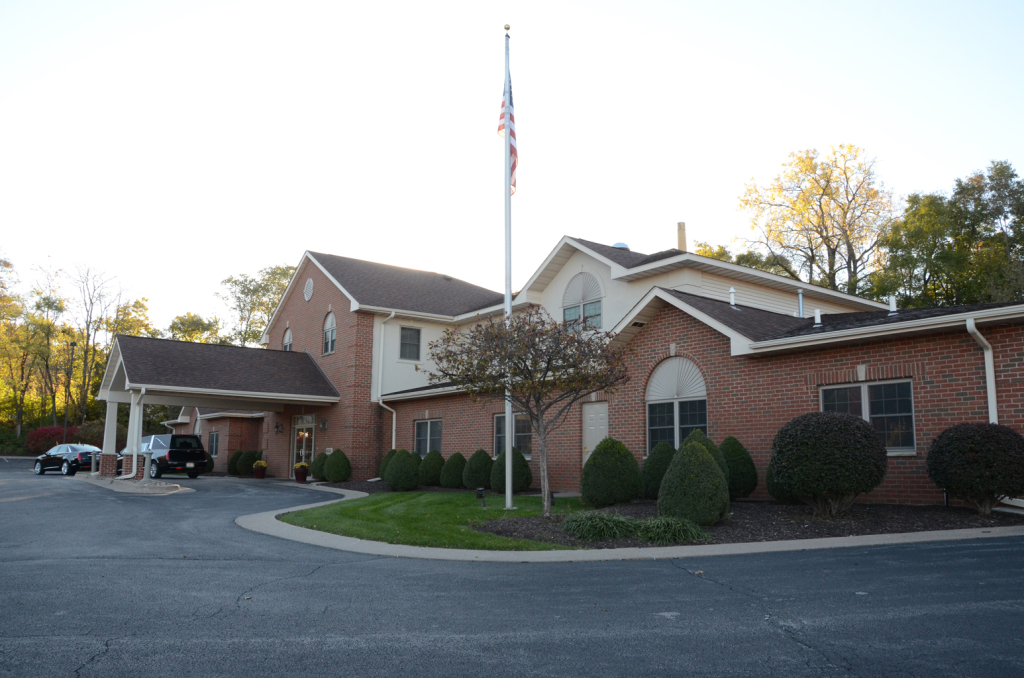 Brick building with a covered entrance, American flag, and surrounding landscaping.