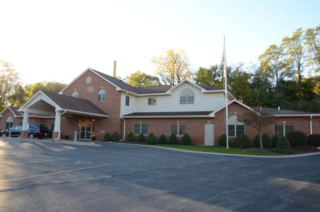 Brick building with a covered entrance and American flag; likely a business or facility, set in the outdoors.