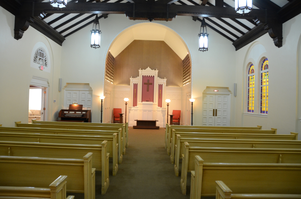 Interior of a church with wooden pews, altar, and stained-glass windows.