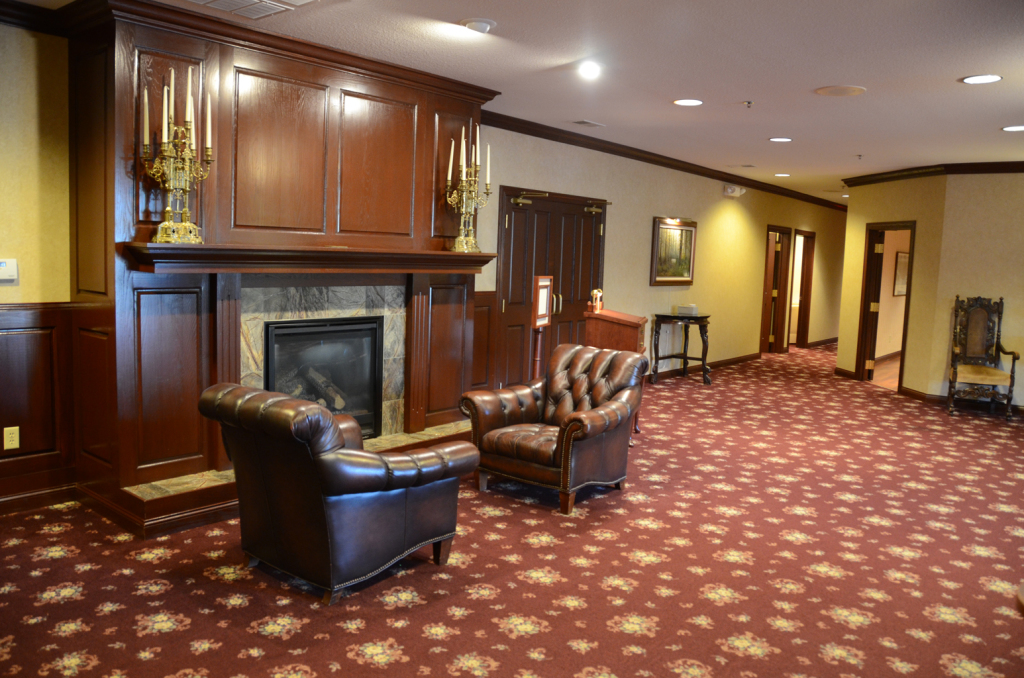 Two leather armchairs sit before a fireplace in a room with patterned red carpet.