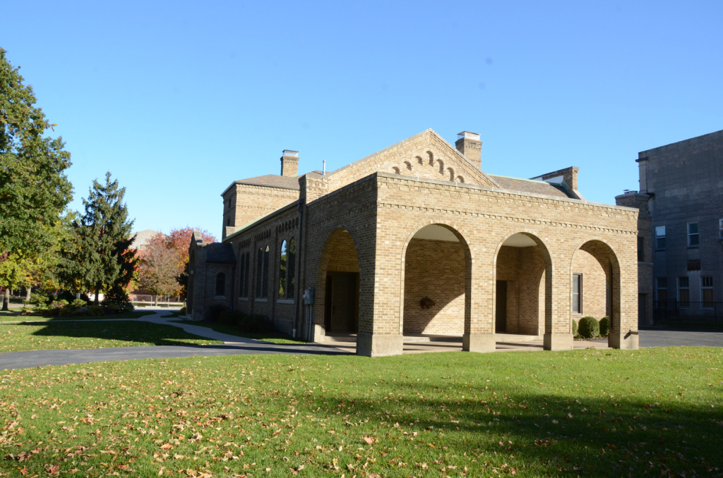 Stone building with arched entrance and green lawn on a sunny day.