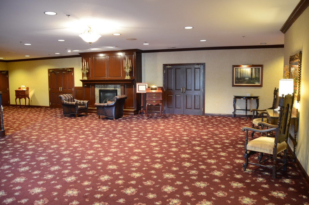 Spacious room with floral carpet, fireplace, chairs, and double doors.