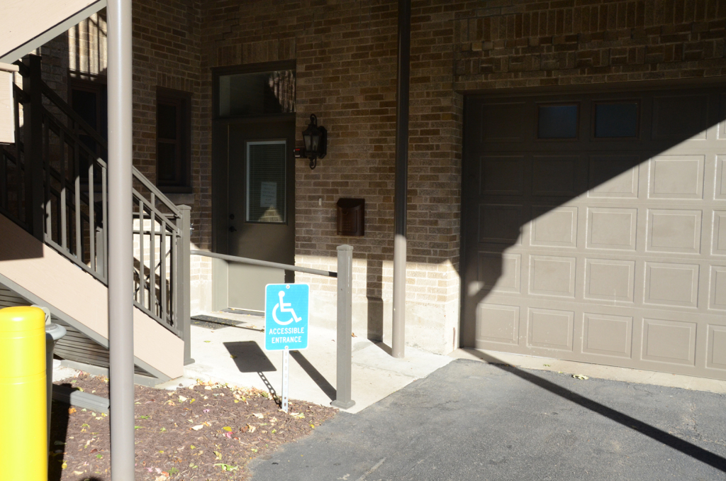 Exterior view of building with accessible entrance, ramp, and garage door. Blue wheelchair symbol sign.