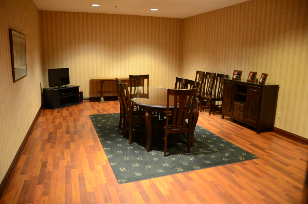 Empty dining room with wooden furniture and flooring, patterned wallpaper, and a blue rug.