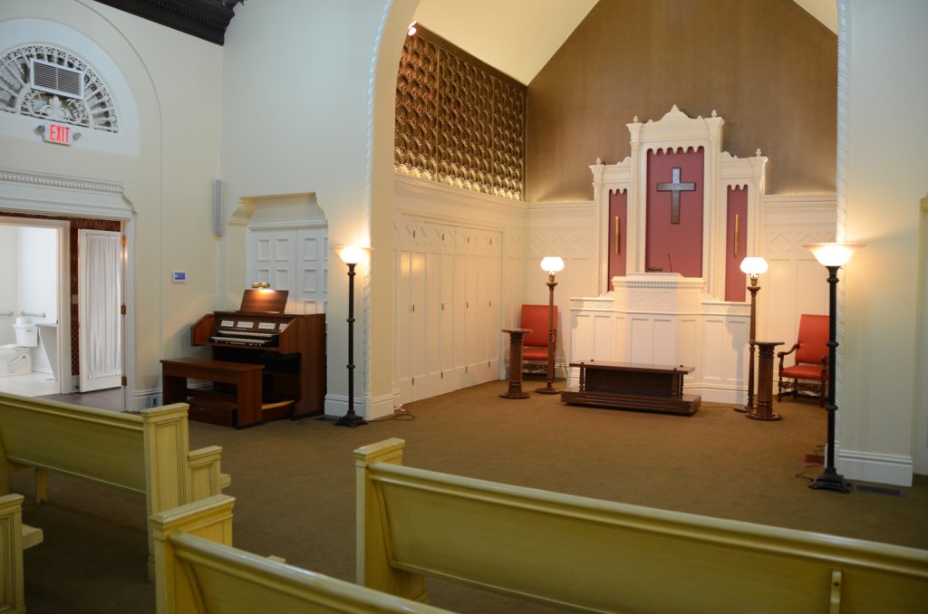 Interior church with altar, organ, pews, and lamps.