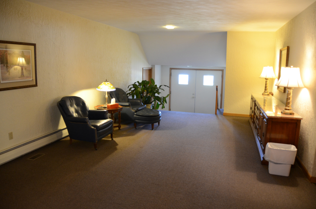 Hallway with seating and lamps, leading to double doors, with artwork and a side table.