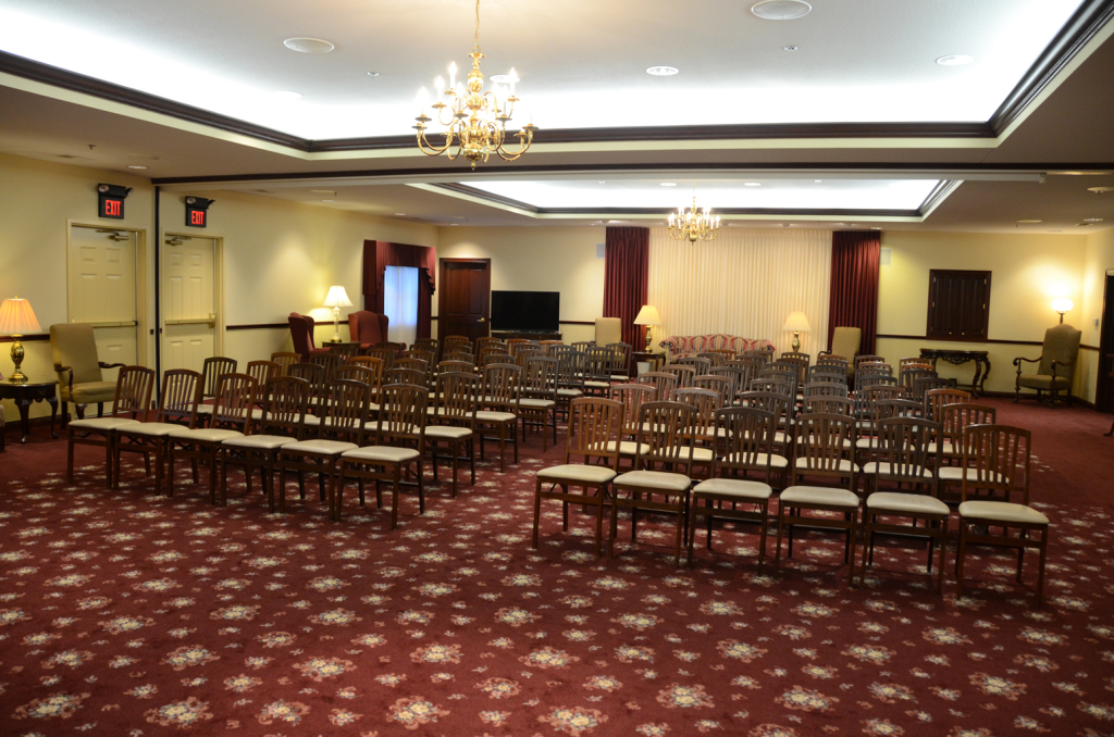 Rows of chairs set up in a room with red patterned carpet, chandeliers, and a stage.