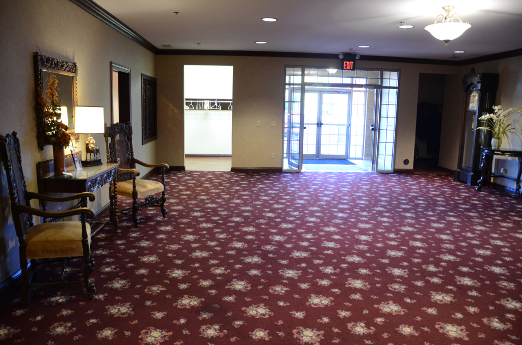 Hallway with red patterned carpet, antique chairs, and an open doorway.