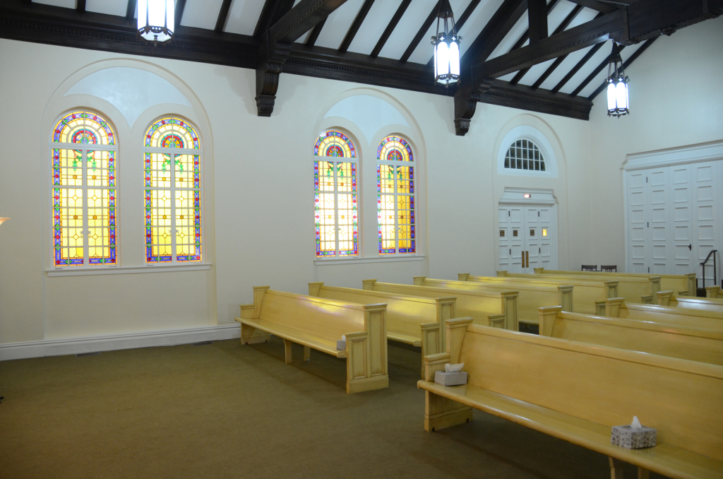 Interior of a chapel with stained glass windows and wooden pews. The ceiling has dark wooden beams.