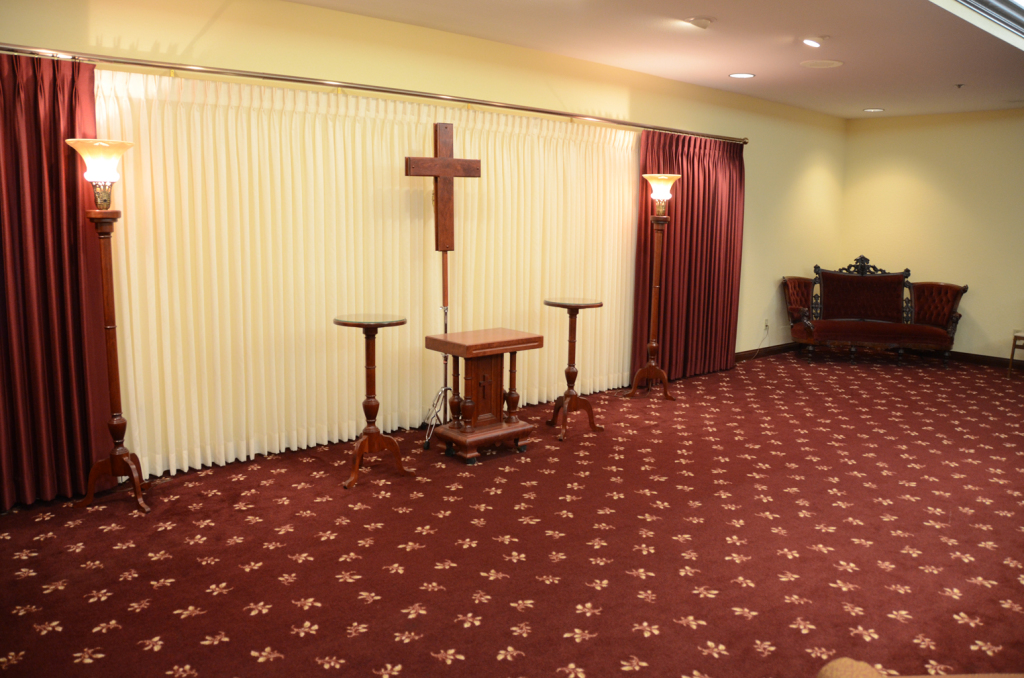 Funeral home interior with burgundy carpet, a wooden cross, and seating.