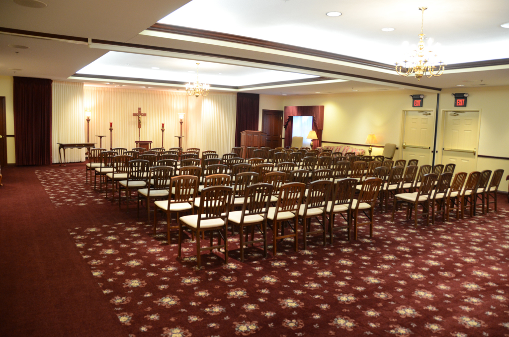 Rows of chairs face a wooden altar in a room with red patterned carpet and a cross.