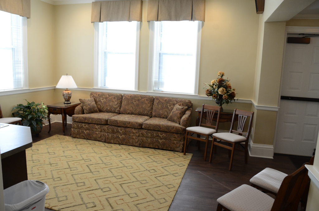 Waiting room with sofa, chairs, rug, and windows.