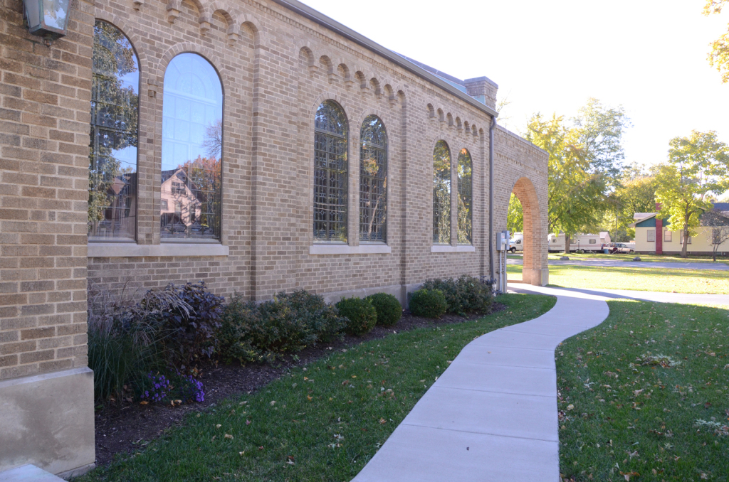 Tan brick building with arched windows, curved walkway, and green grass.