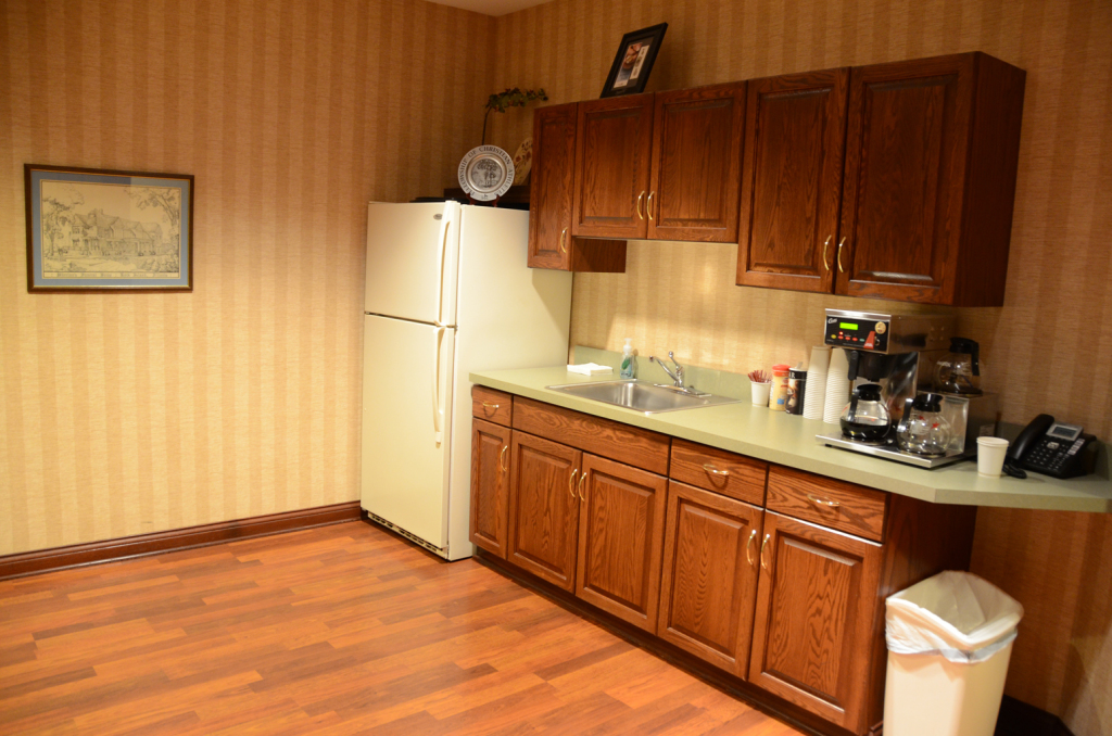 Office kitchenette with cabinets, appliances, and waste bin.