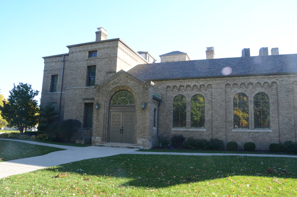 Brick building with arched doorway and multiple windows on a grassy lawn with a path.