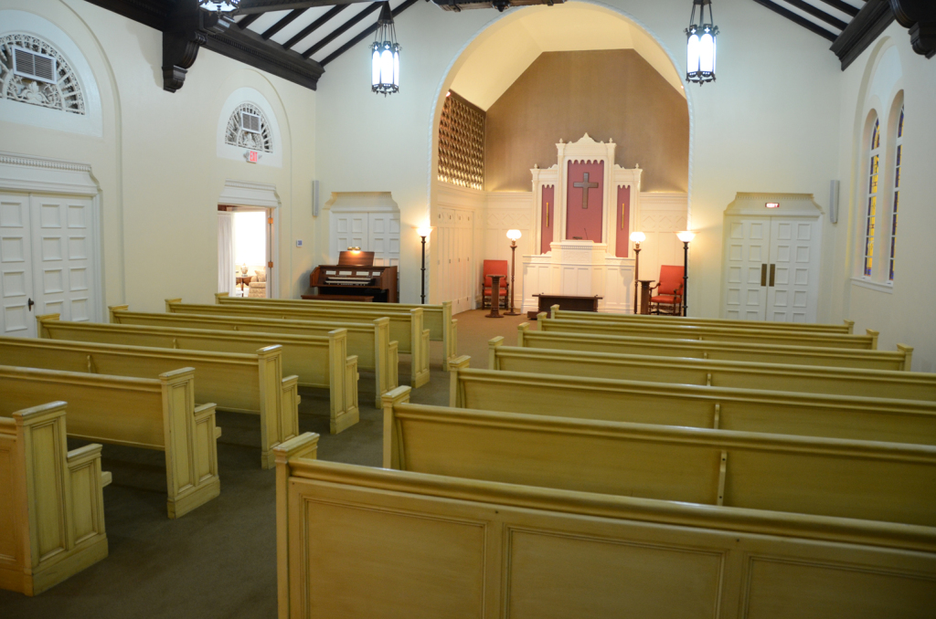 Interior of a church sanctuary with pews, altar, and stained-glass windows.