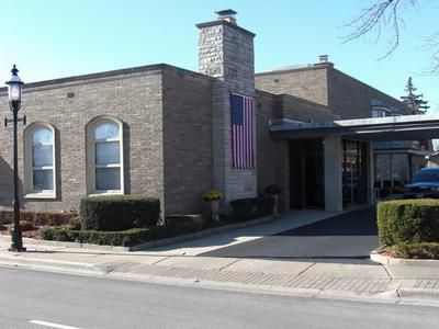 Brick building with arched windows, a stone chimney, and an American flag by the street.