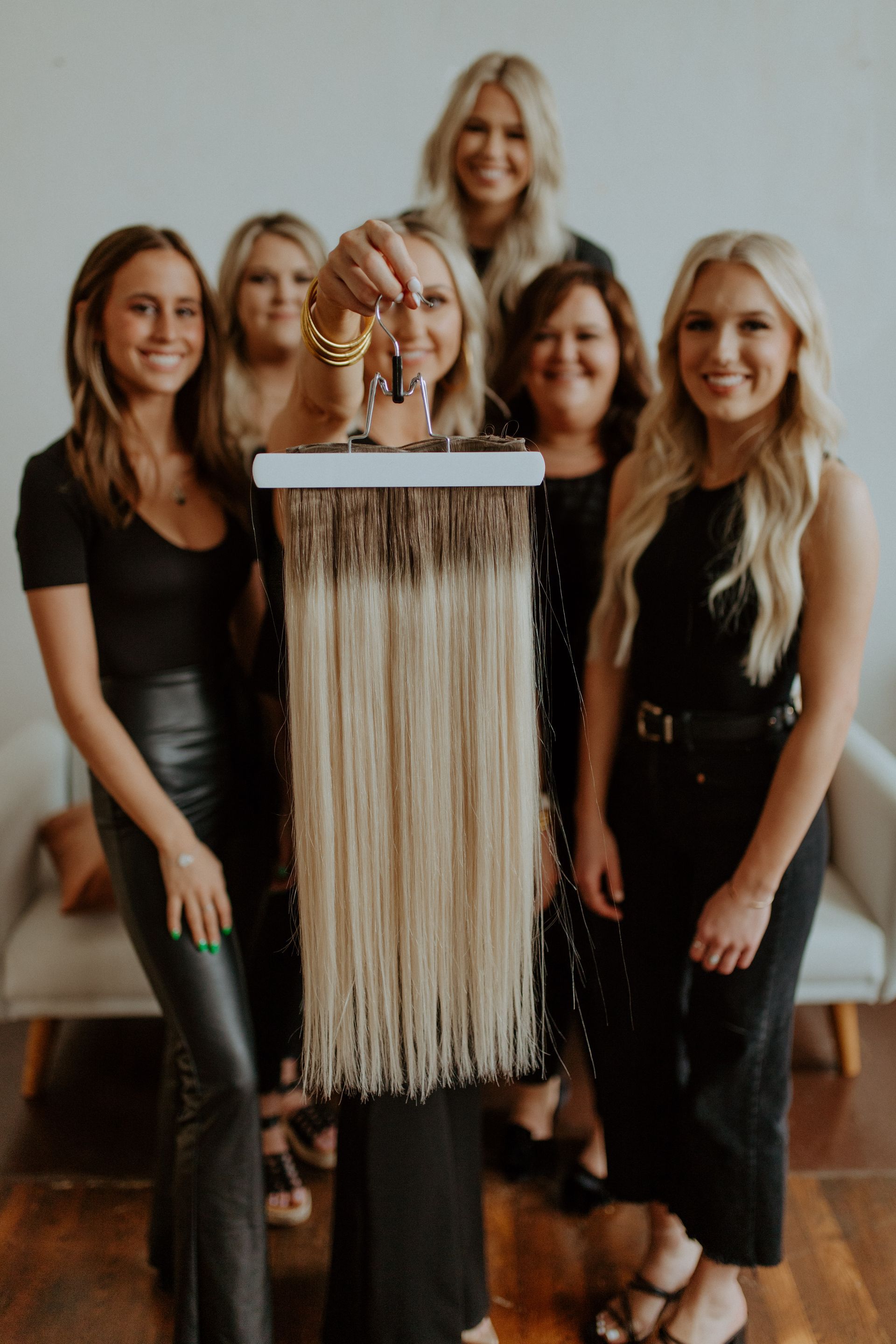 Group of women holding hair extensions, smiling. Blonde and brunette hair in a modern setting.