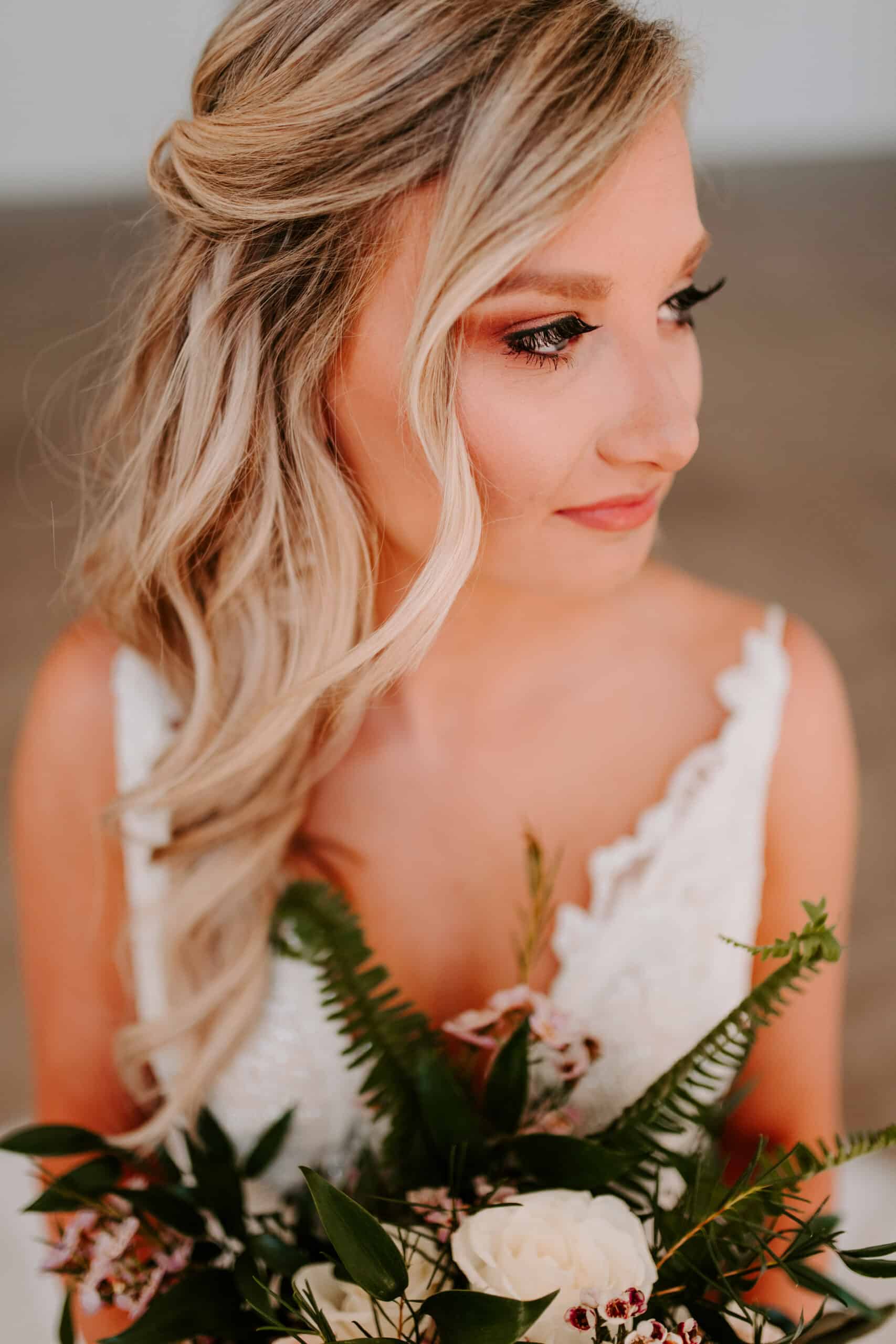 Blonde woman in a wedding dress, holding a bouquet. She looks to the side with a soft smile.