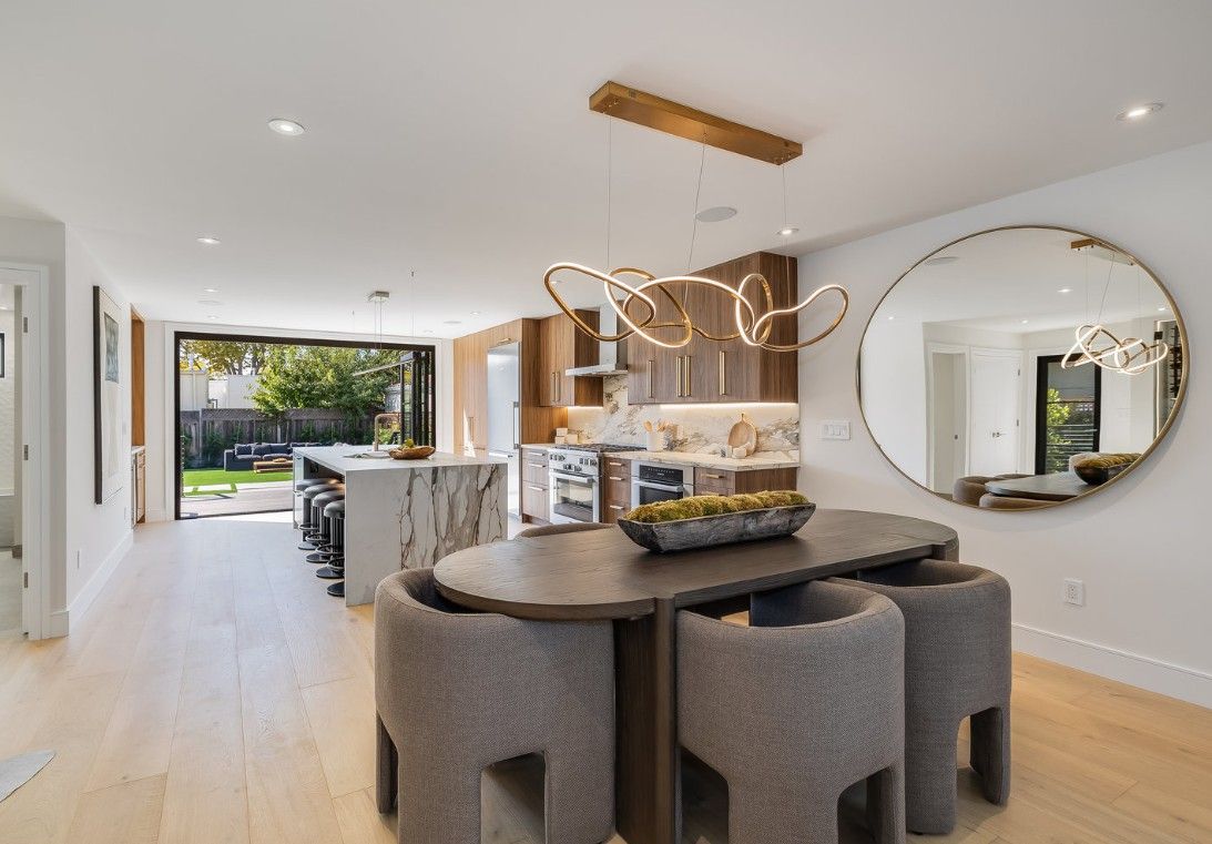 Modern kitchen and dining room with a marble island, oval table, and large mirror.