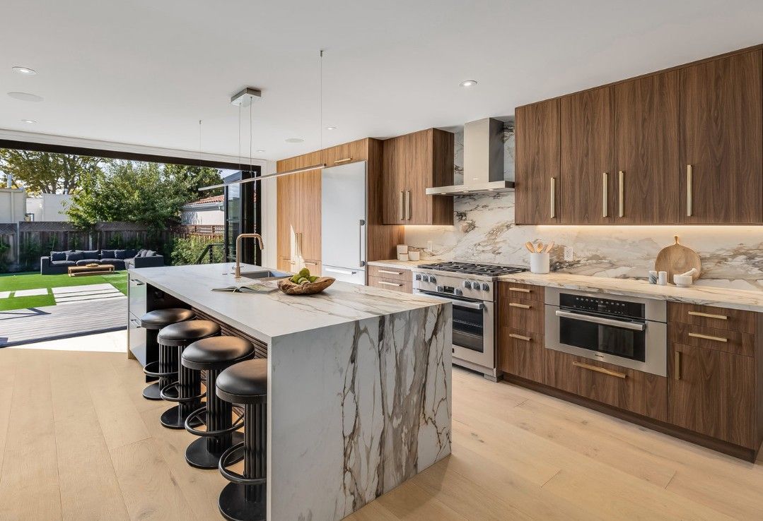 Modern kitchen with marble island, wood cabinets, and backyard view.
