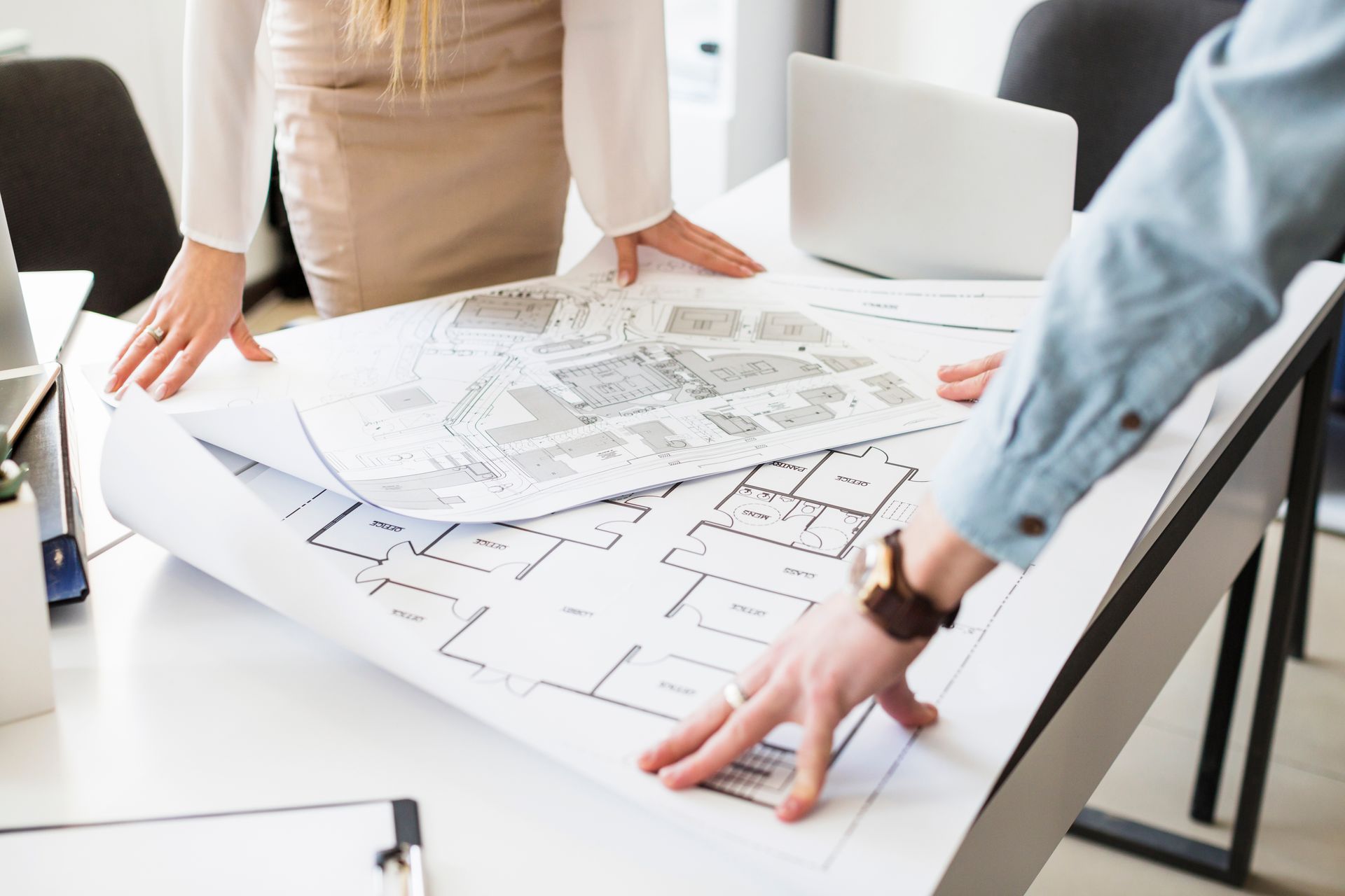 A man and a woman are looking at a blueprint on a table.