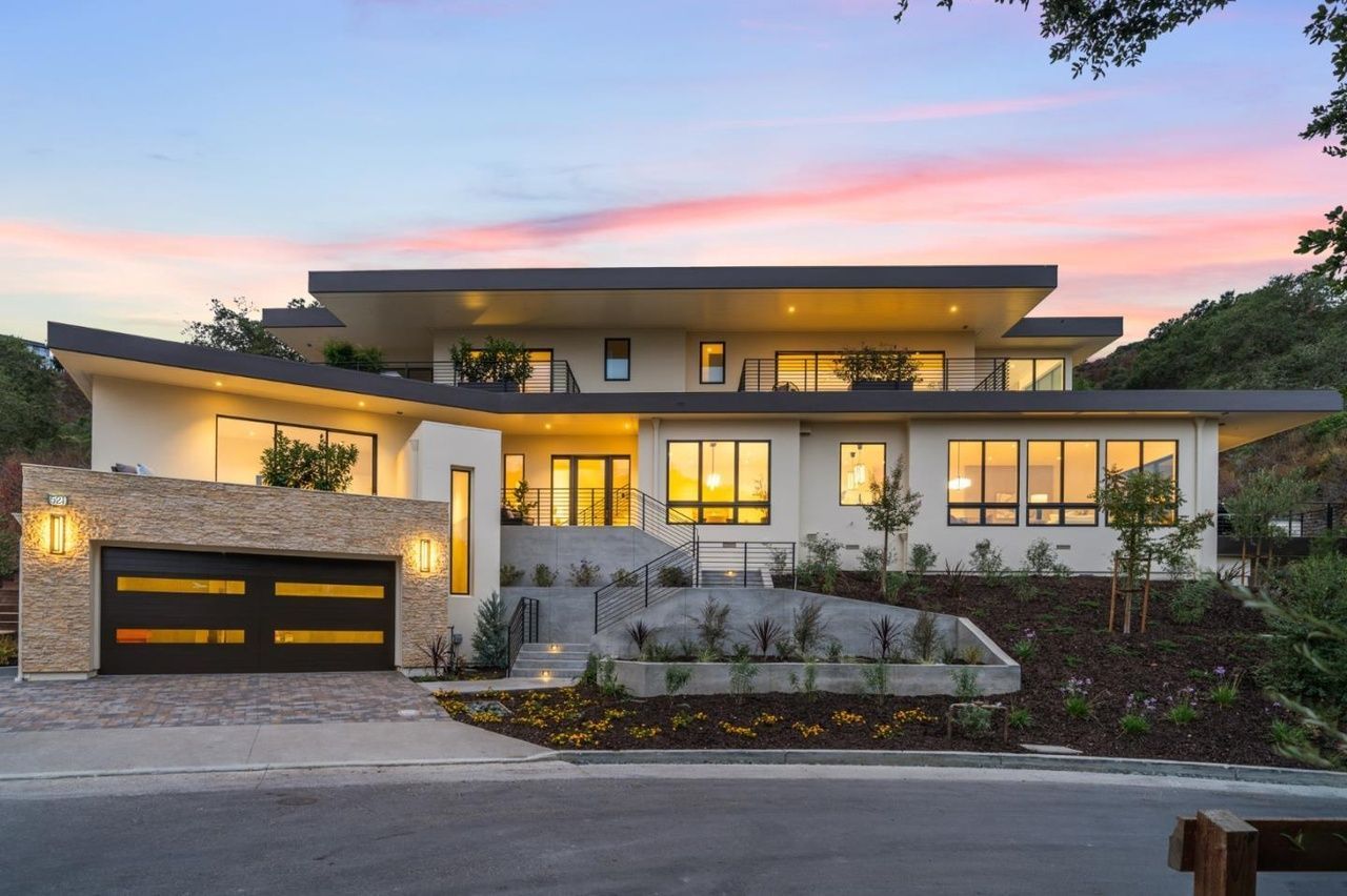 A large white house with a black garage door is sitting on top of a hill.