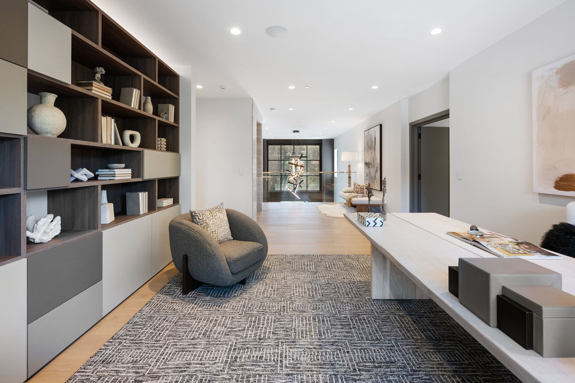 A living room with a chair , desk , shelves and a rug.