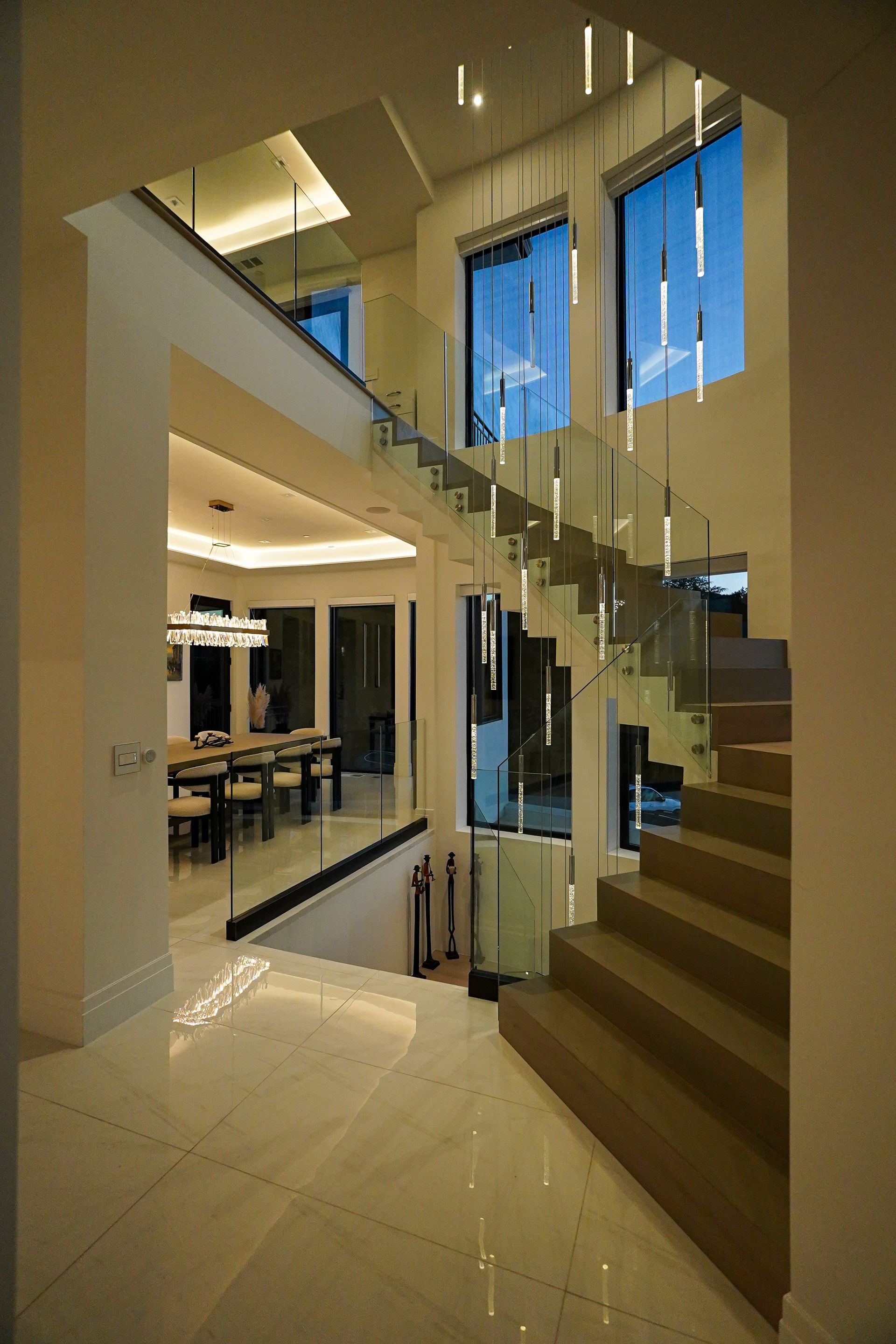 A staircase with a glass railing and a dining room in the background