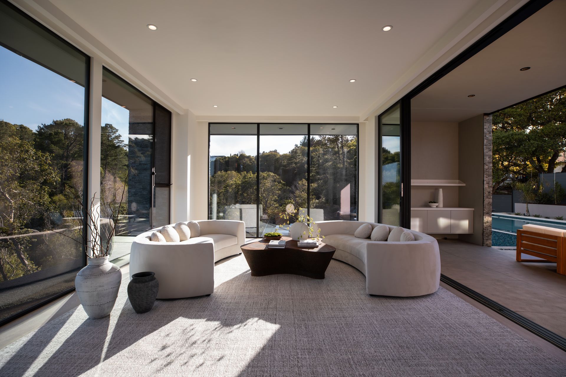 Living room with large windows, curved white sofas, and a view of trees.