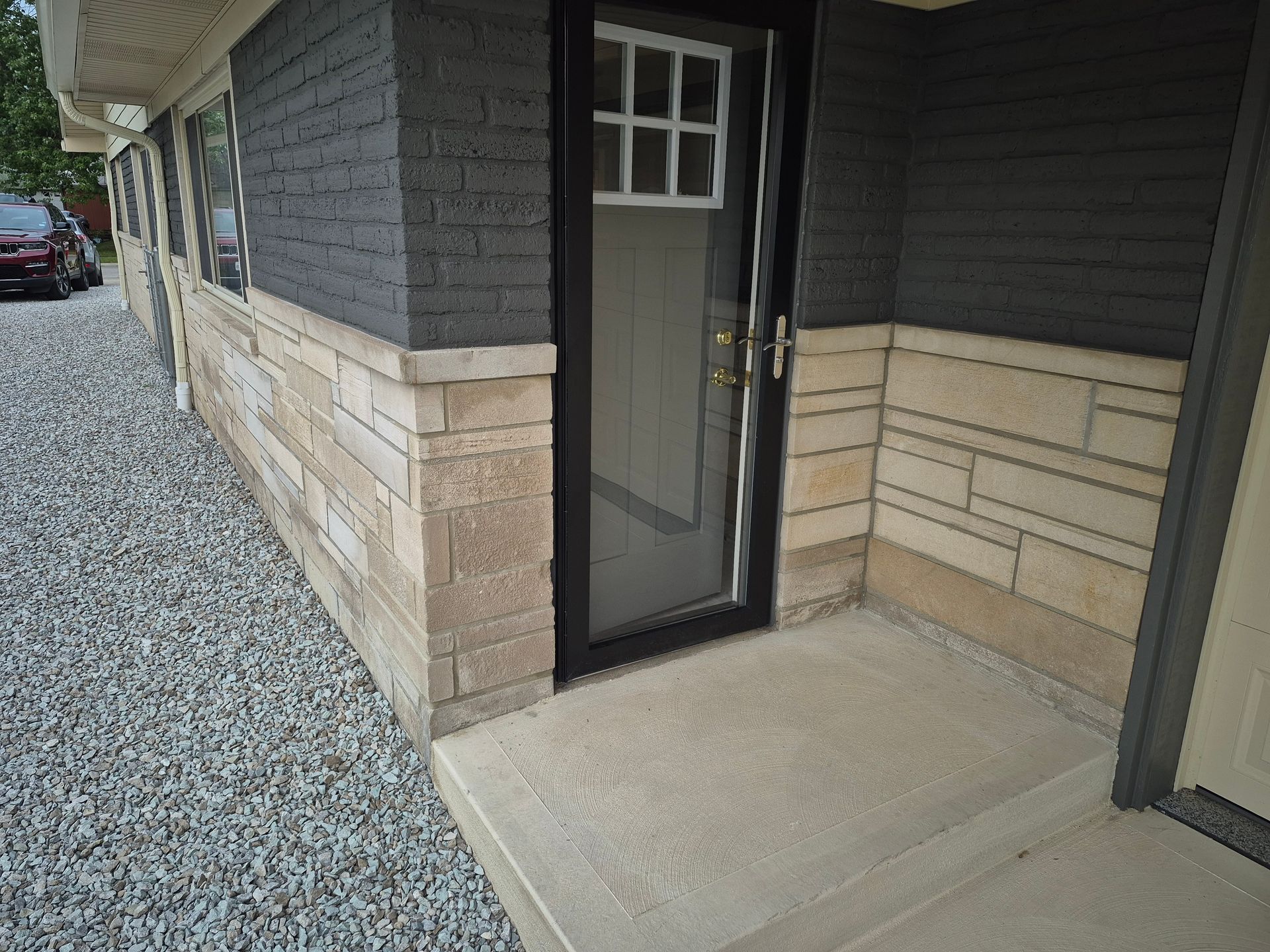 Exterior of building with stone facade, door, and concrete entrance. Gravel driveway.