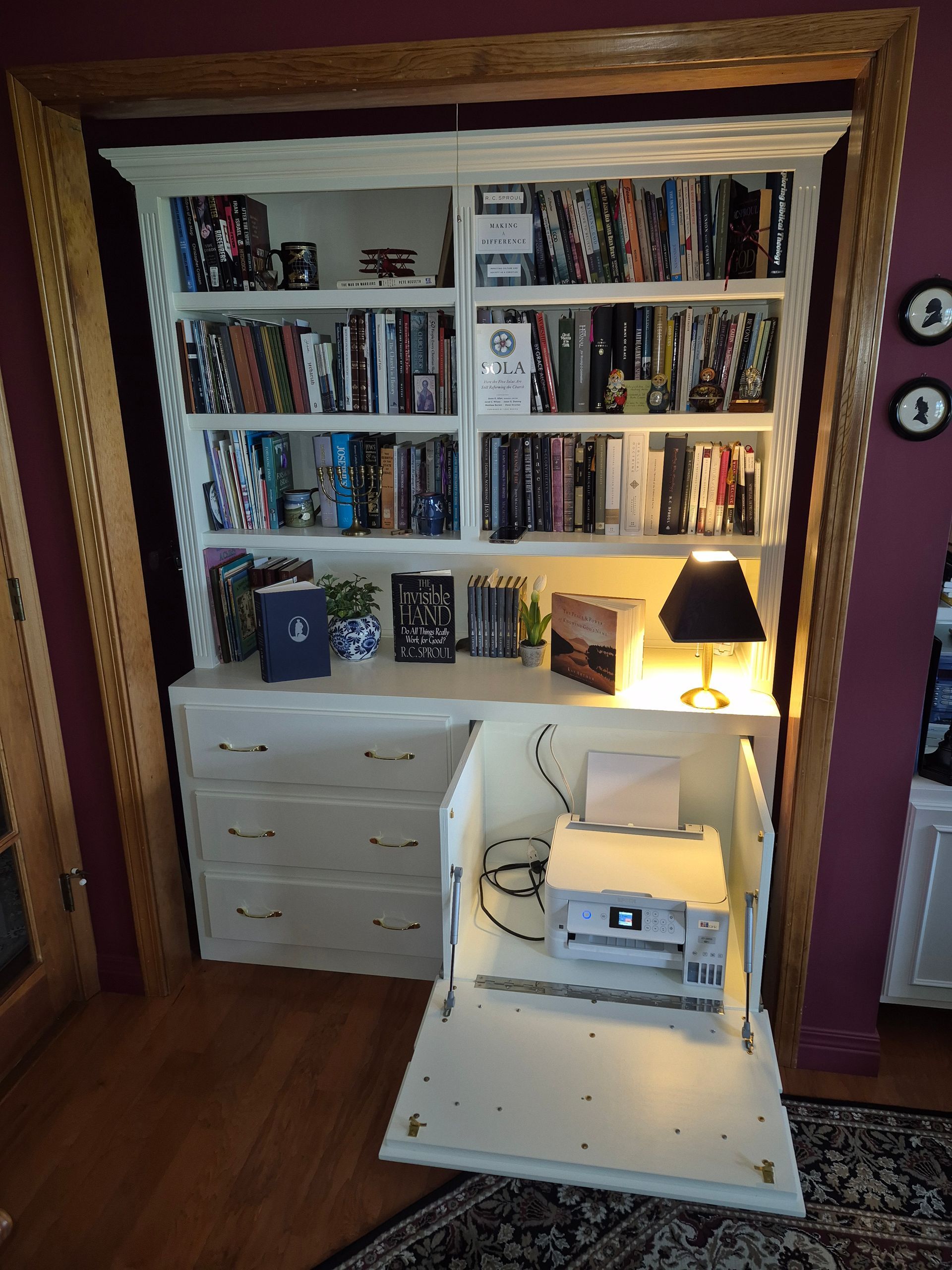 Built-in white bookshelf with books, drawers, and a lit lamp in a cozy room nook