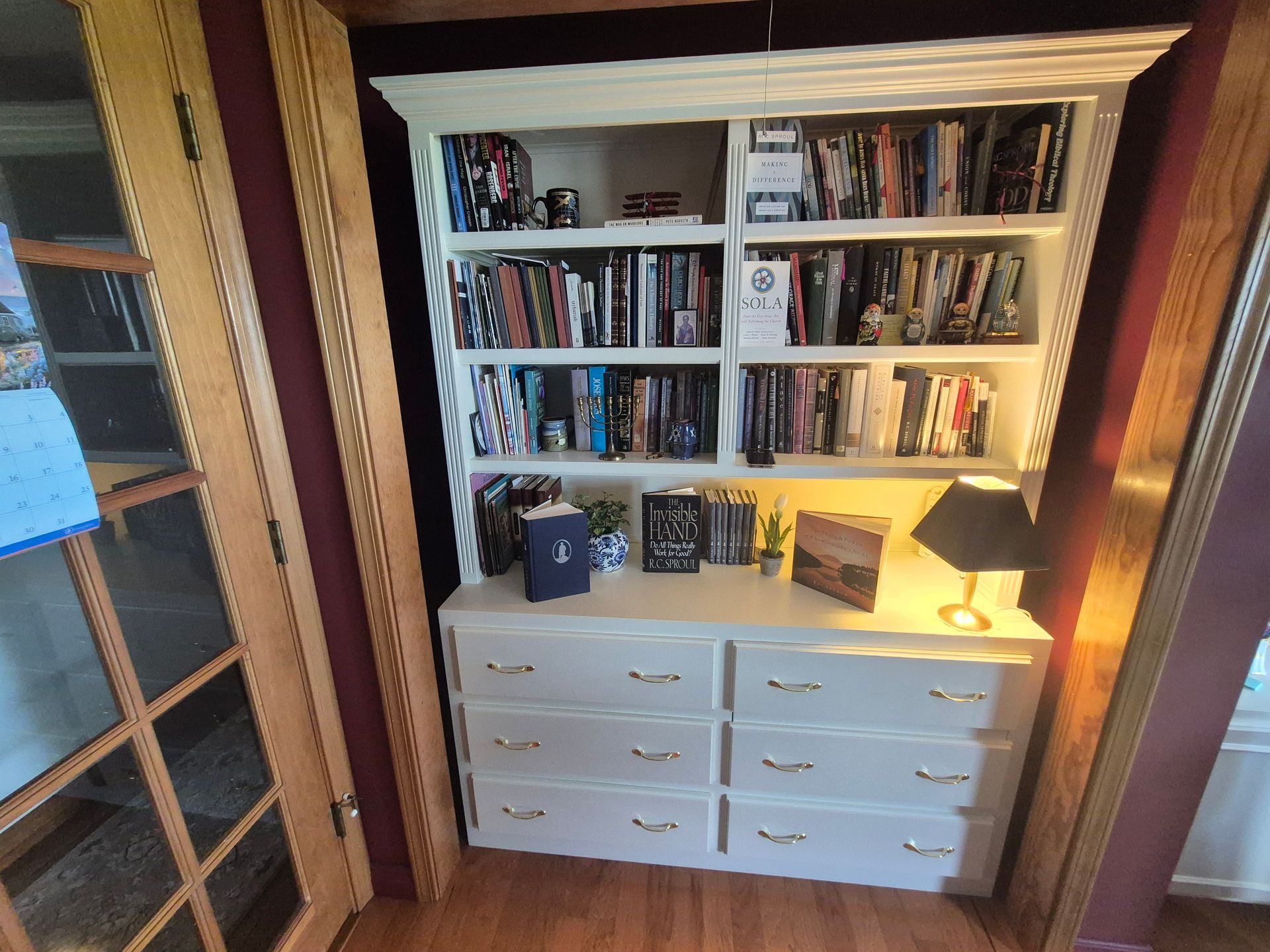 Built-in bookshelf and white dresser in a doorway, filled with books and lit by a warm lamp