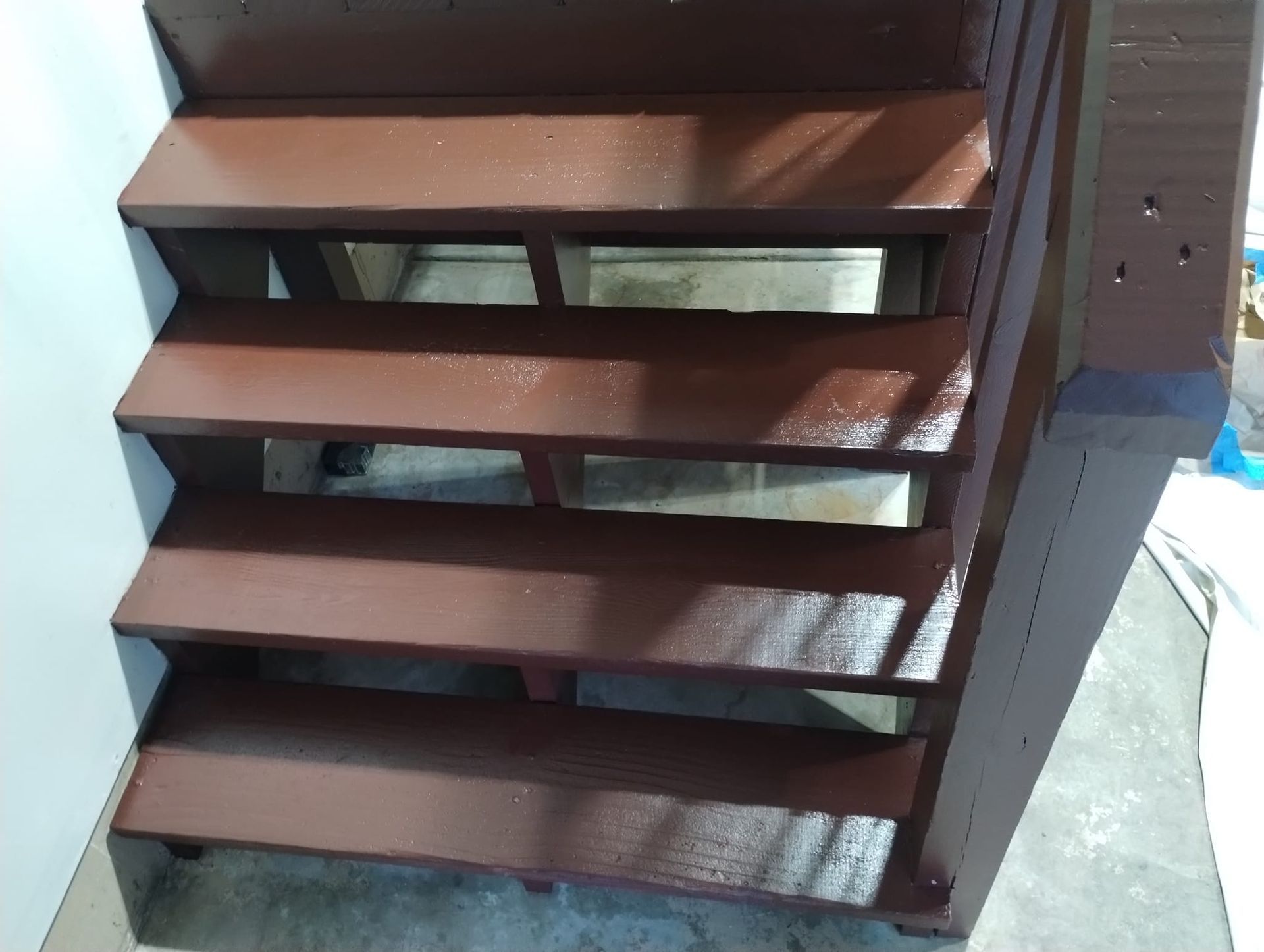 Brown painted wooden stairs with open risers against a white wall and dark wood frame.
