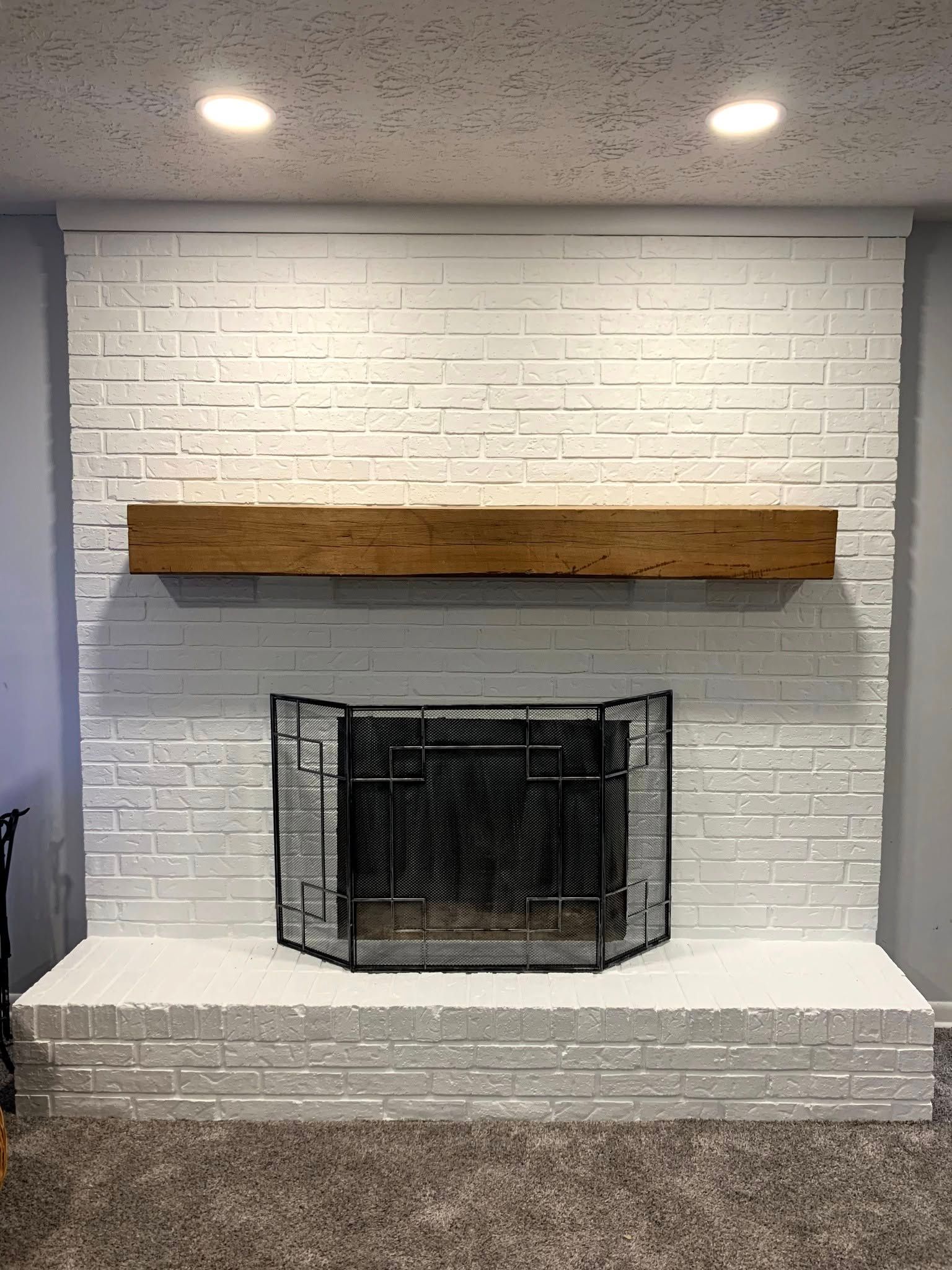White painted brick fireplace with a wooden beam mantel and black fire screen.
