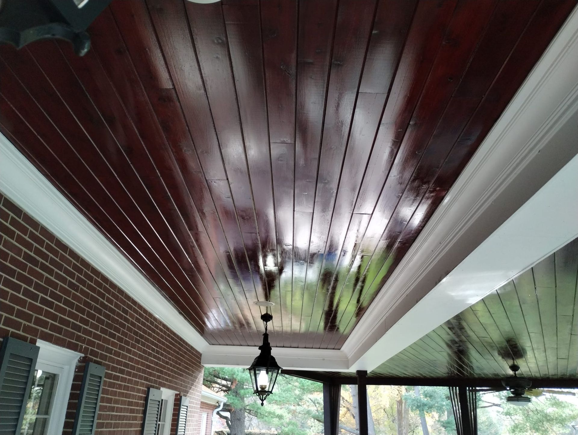 Dark wood ceiling with white trim and a hanging light on a porch. Brick wall visible.