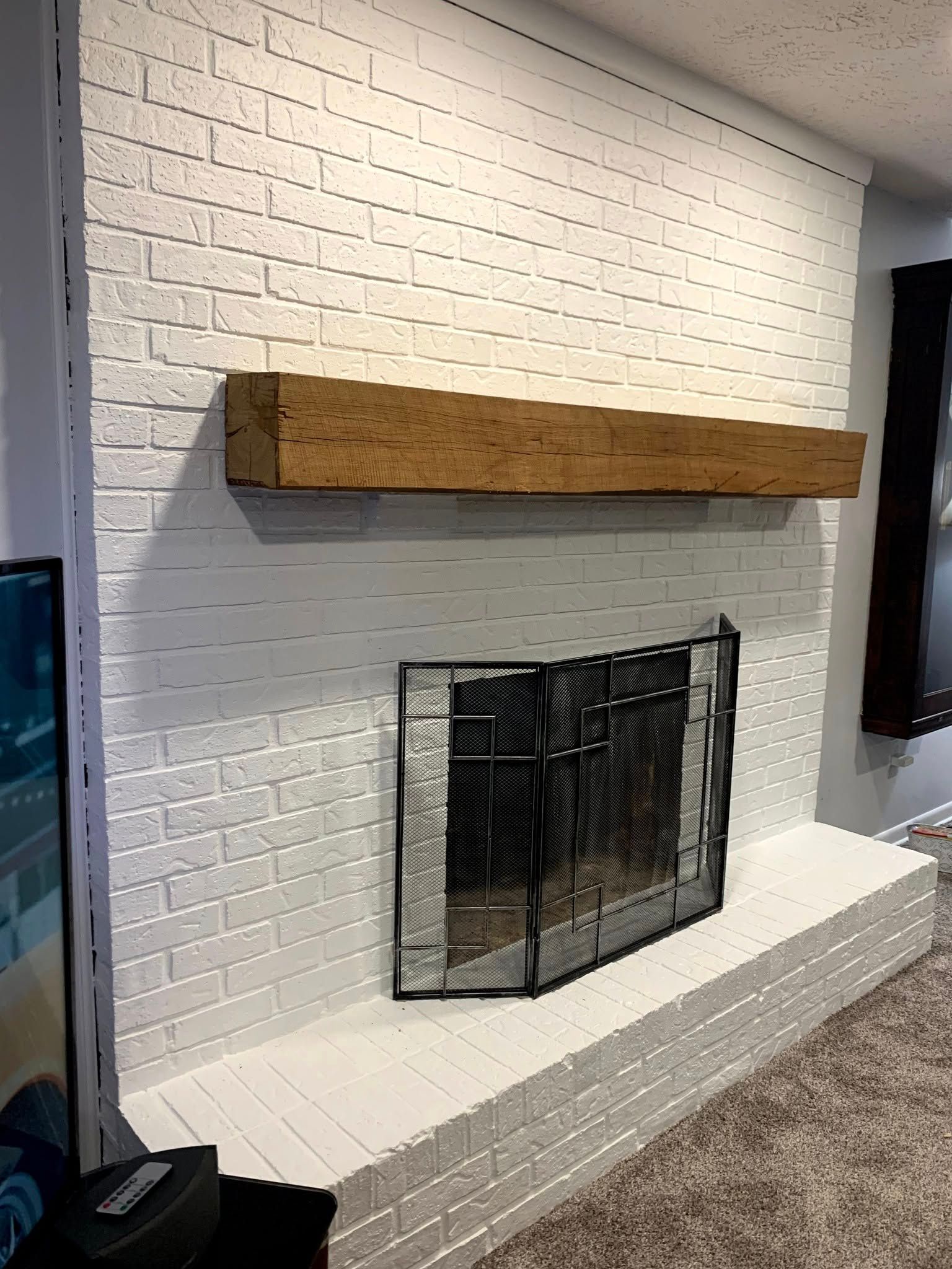 White brick fireplace with wooden mantel and black screen.