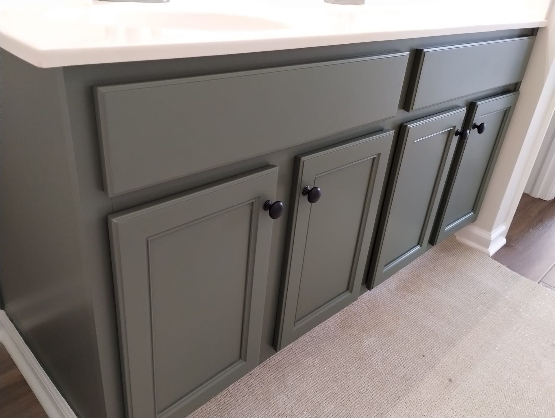 Green bathroom vanity with black knobs and a white countertop.