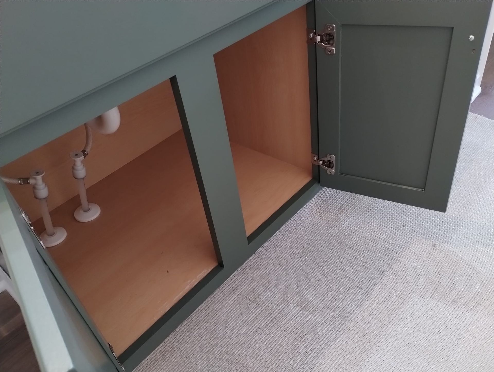 Open green bathroom cabinet with plumbing visible.