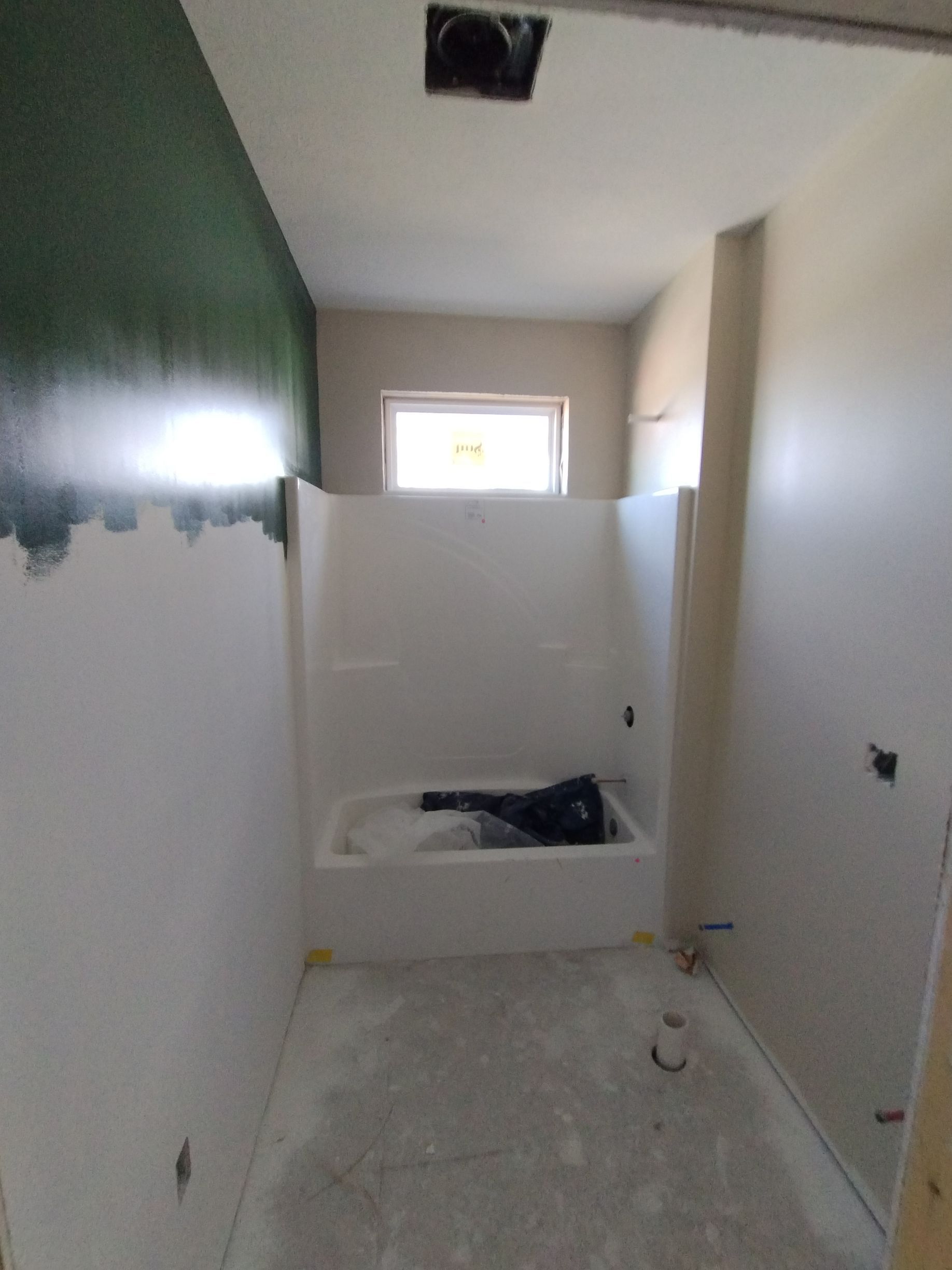 Bathroom under construction; white walls and tub; green wall on left; natural light from window.