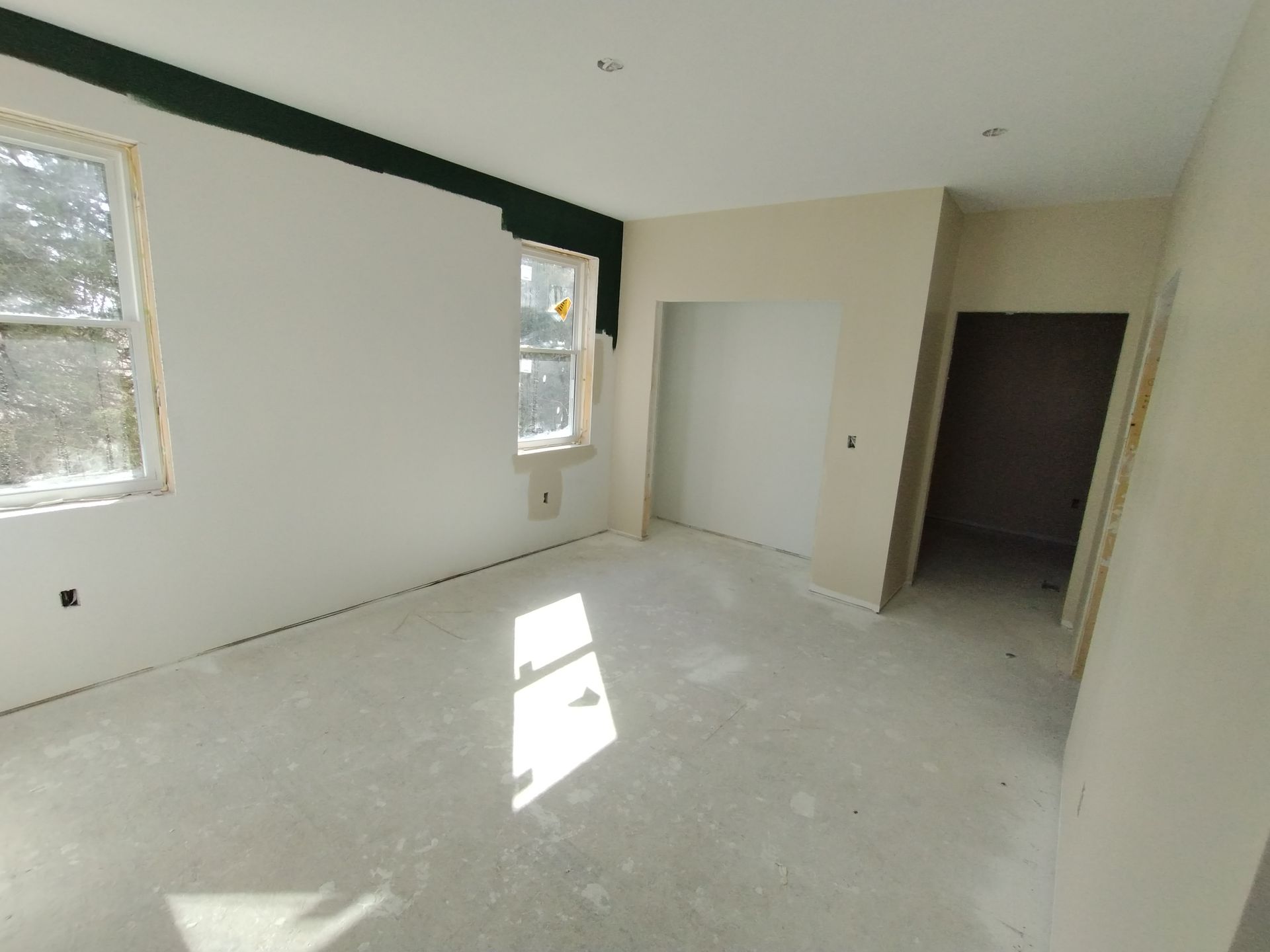 Empty room under construction with two windows and an open doorway.
