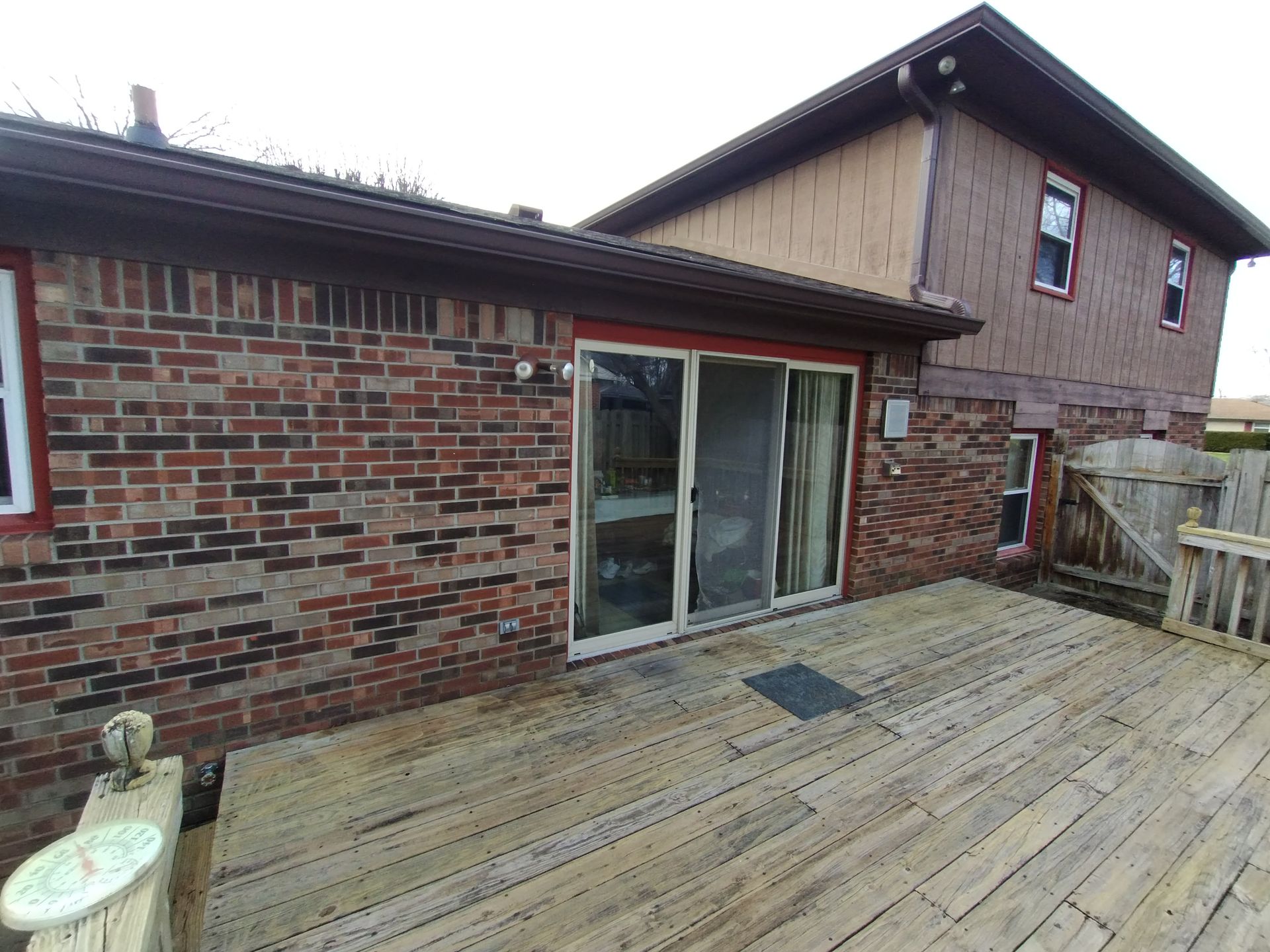 Brick house with deck, sliding glass door, brown wood siding, and wooden fence in the background.