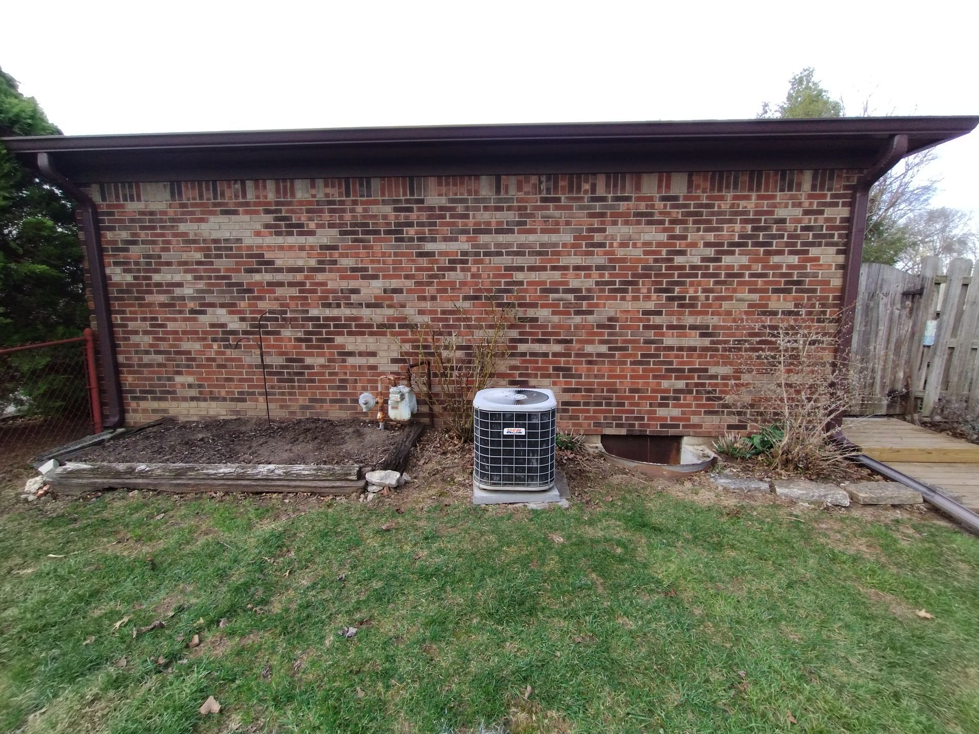 Brick building exterior with air conditioner, grass, and small garden.