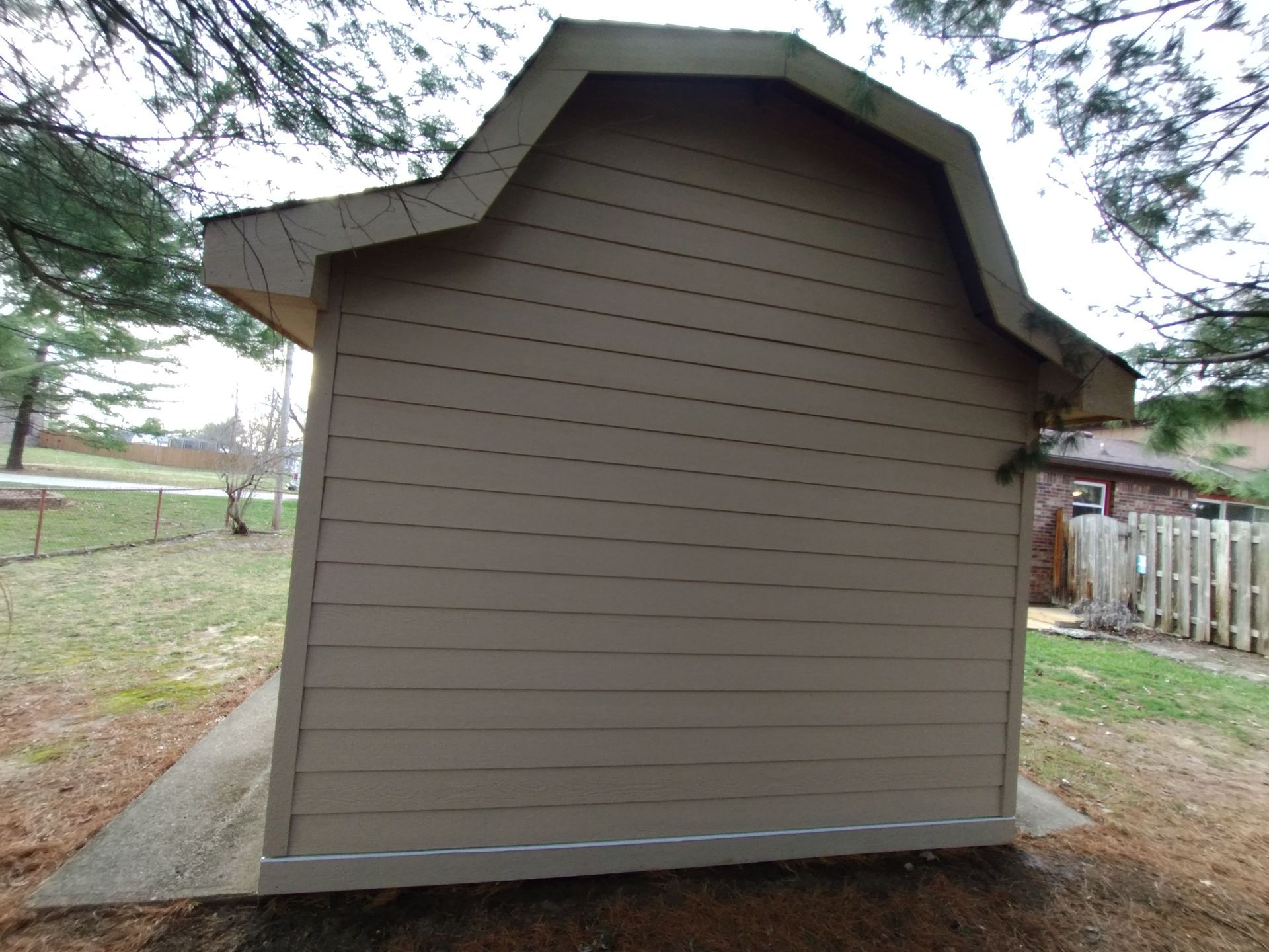 Tan shed with a unique roof design, set on a concrete slab.