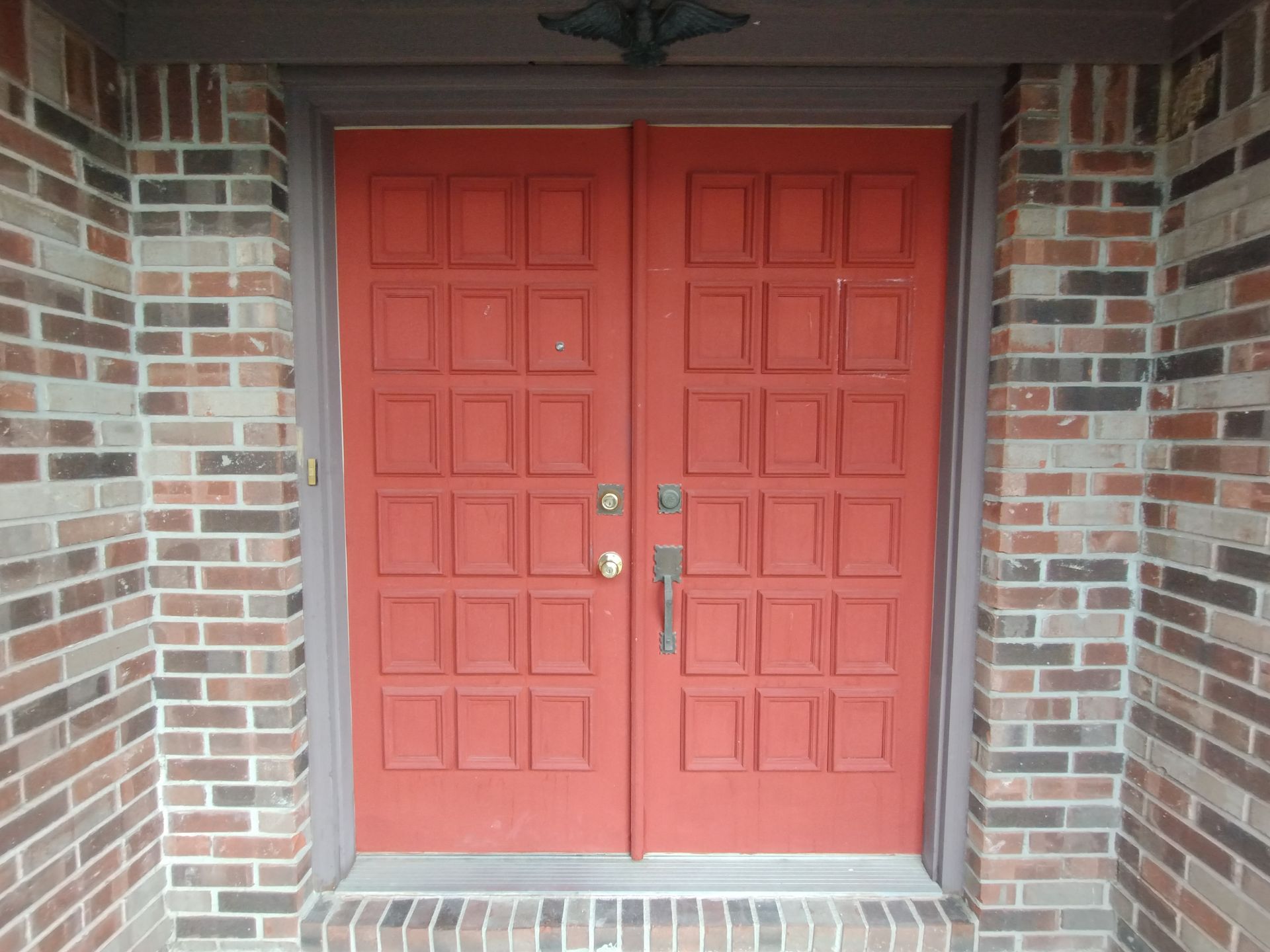 Red double doors with a grid pattern, set in a brick entryway.