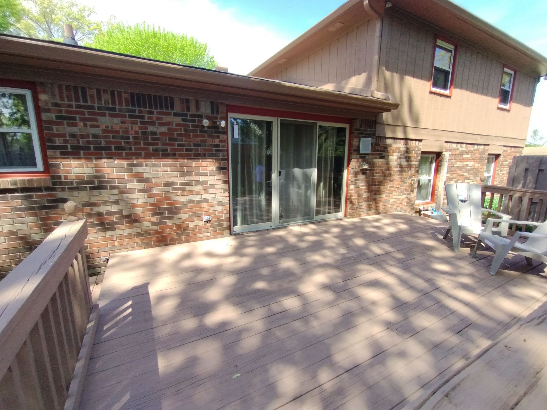 Back deck with a brown wood surface and a brick and wood-sided house. Sliding glass doors lead indoors.