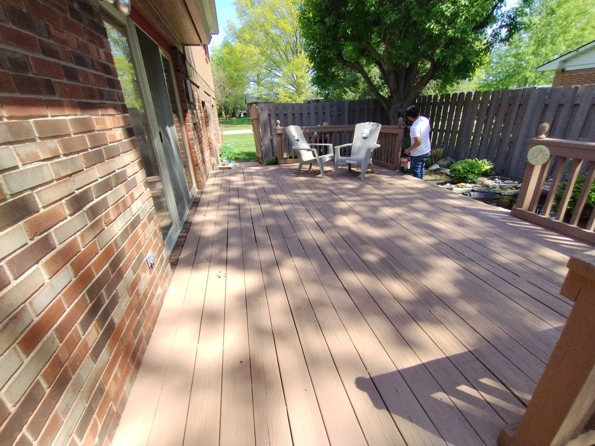 A wooden deck next to a brick wall with a person standing near a fence in the background.