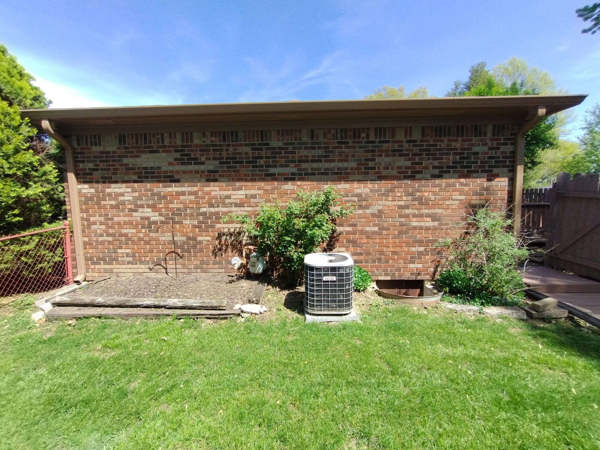 Brick wall with AC unit, surrounded by grass and plants on a sunny day.
