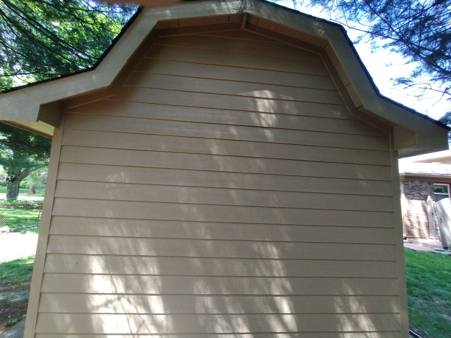 Tan shed with a gabled roof against a blue sky.